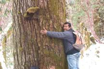 Photo shows a man hugging a big tree trunk.