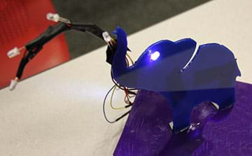 A photograph shows a blue 3D-printed elephant sculpture with LEDs in its eye sockets (2) and on wires (4) that are arcing out of its trunk.