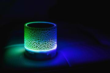 A photograph taken in darkness shows a cylindrical night-light with a crackle finished that glows green and blue.