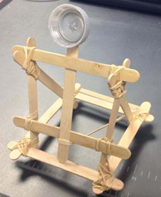 A photograph shows a small catapult structure made from Popsicle sticks, rubber bands and a plastic bottle cap.