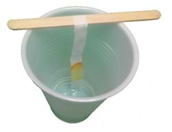 Procedure set-up. Photo of a popsicle stick balancing on the top of a paper cup, supporting a strip of coffee filter, hanging down in the cup and touching the liquid at the bottom of the cup. The lower part of the strip is colored from components of the ink rising up the filter along with the liquid.