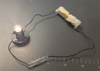 A photograph shows a simple circuit with a battery, light bulb and paper clip.