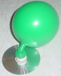 A photograph of a model hovercraft; a blown up balloon is attached to a bottle cap, which is glued to a CD.