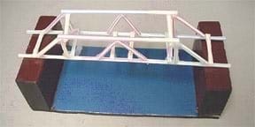 A photograph shows a truss-style straw bridge (Howe-Kingpost design) made of plastic drinking straws and clear tape spanning the gap between two wooden blocks, ready for testing.