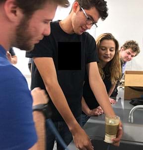 Four students set up a quicksand experiment over a lab sink using the vacuum filter with three students observing. 