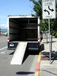 A photograph shows the back of a big truck with a ramp from the road up to the interior floor of the truck.