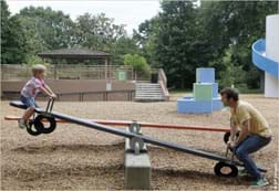 A photograph shows a playground see-saw with a boy at one end, up in the air, and a man at the other, lower end of the long plank.