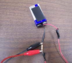 Photo shows a 9V battery connected by wire to a resistor placed between two probe leads (red and black).