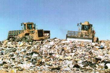 A photograph of a modern landfill - two bulldozers push around a huge pile of trash.