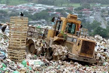 Photo shows a heavy piece of machinery driving over a landfill.