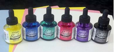 A photograph shows six small glass bottles Dr. Ph Martin's Bombay India ink: yellow, blue, green, red, purple, black. Each bottle has a black squeezable eye dropper as part of its screw-on cap, which can be used to distribute ink drops. Also shown is an assortment of light colored, inexpensive sheets of construction paper (pink, yellow, light blue, white).