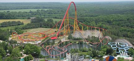 A wide photograph shows an aerial view of the entire Intimidator 305 roller coaster at Kings Dominion theme park, VA. The track route includes curves and loops over land and water with one very high climb and drop in the center of it all.