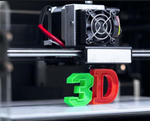 A photo of a 3D printer head tool with two printed plastic examples below; a green “3” and a red “D”.