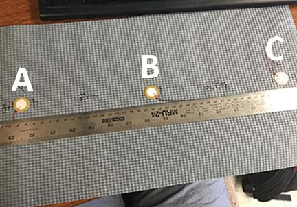 A photograph shows a gray rubber mat with three piezoelectric transducers (each looks like a small white circle with an attached wire) attached in a line and labeled A, B and C. Transducers A and C are located 3 cm from opposite mat edges with B located between them. All three are located 20 cm from each other. A ruler on the mat shows the distances.