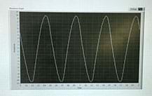 A photograph shows a computer-generated ongoing sign wave displayed on a computer monitor—a curving white line on a black background. The x-axis is time. The y-axis is the amplitude, which suggests the voltage level. 