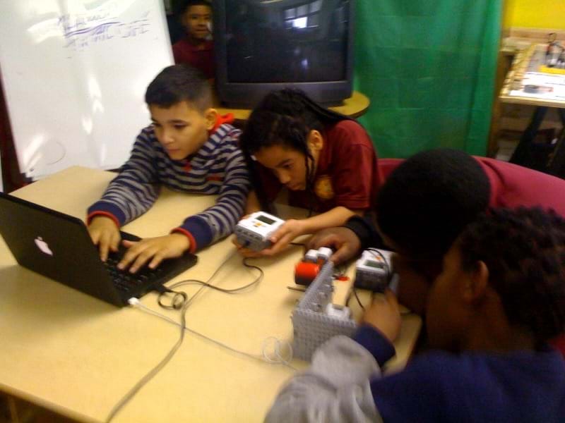 A photograph shows four students at a table working with a laptop, LEGO brick and the experimental setup made from LEGO components.