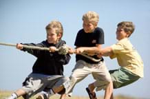 Photo shows three boys pulling on a rope, one half of a tug of war game.