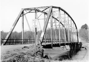 A black and white photo shows a deck bridge, with large trusses on the top of the bridge.