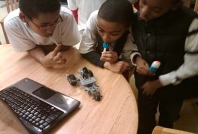 A photo graph of three young boys experimenting with a LEGO vehicle.