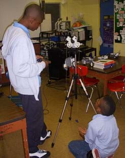 A photograph shows two boys in a classroom near a tripod with a device four-wheeled LEGO device mounted on it. Source/Rights: 2012 Jeffrey Laut, AMPS, NYU-Poly 