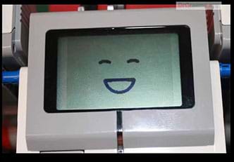 A photo of handheld plastic device with a small display screen and buttons. The display image is a smiley face.