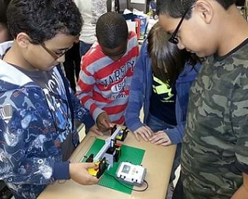 A photograph of four students interacting with the LEGO Balance Scale