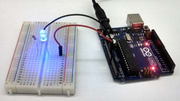 A photograph shows an Arduino Uno microcontroller connected to a clear LED (lighted bulb) via two jumper wires, a breadboard and a resistor.