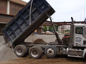 Photo shows a dump truck unloading a load of gravel.