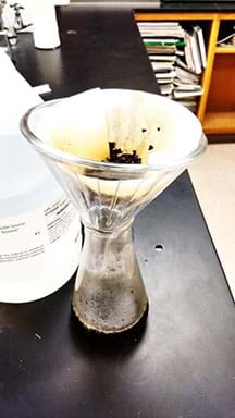 Photo of a funnel filter over a 500 ml flask.  The filter is removing pieces of tea after brewing.