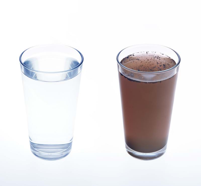A glass of clean, clear water next to a glass of dirty water, photographed on a white background. 