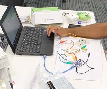 A photograph shows a student’s arm as he codes the Circuit Playground to work with the visible circuit.