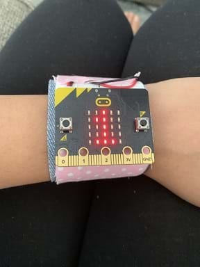 A micro: bit pedometer is worn on a person’s wrist. The pedometer has a digital display in red showing the number 1. 