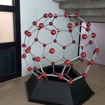 A photograph of a large three-dimensional ball-and-stick model of a buckyball, a carbon-60 molecule, sitting on a support stand.