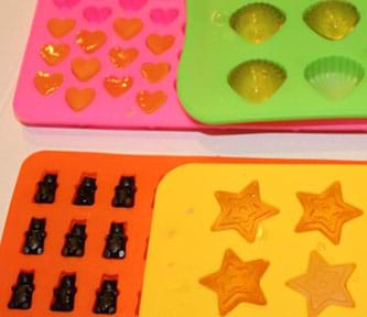 An image of hydrogels prepared in molds of different sizes, shapes, and colors. The hydrogels are yellow, orange, and blue while the molds are made up of pink hearts, lime green shells, orange gummi bears, and yellow stars.  
