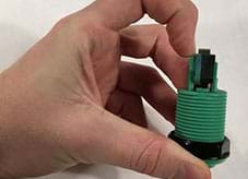 A photograph shows a hand positioned to remove a plastic clip from one end of a threaded green and black plastic device.