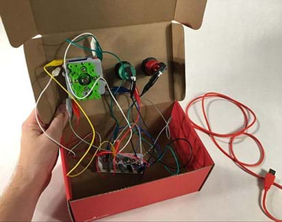 A photograph shows the inside of the shoebox, displaying the undersides of the joystick and two arcade buttons amidst a mass of alligator clip wires and one USB cable.