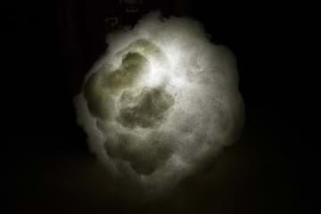 A photograph taken in a dark room shows a paper lantern orb that is entirely obscured by glued-on white fluffy polyfil material and lit by a flashlight held in the center of the lantern/cloud. 