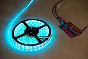 A photograph shows an Arduino on a tabletop next to an illuminated string of blue LED lights coiled on a reel.