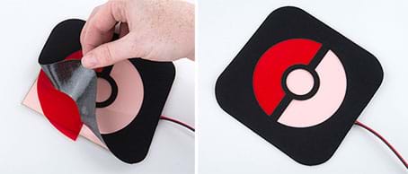 Two photographs. A left, a hand lays the cutout black fabric stencil (with rounded corners) onto the square EL panel over a piece of thin red translucent plastic material that is placed over part of the stencil, positioned specifically to lie under one cutout area. At right, the finished stencil graphic on the EL panel composes a Poke ball, which looks like a circle split in half horizontally with its top half red, bottom half white, and a white center button, entirely bordered by black.