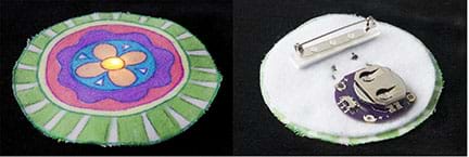 A photograph shows the front and back of a completed, three-inch circle-shaped pin. On the left, the front, a LED light shines through the center of a colorful flower design on white fabric. On the right, the finished back of the pin shows a disc battery in its holder, conductive thread tracers, and a safety pin-type fastener for clothing attachment. 