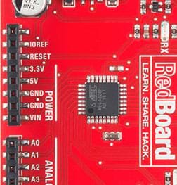 A photograph shows a close up of the SparkFun RedBoard so that you can see black lines (traces) from its center black square chip—its different pins.