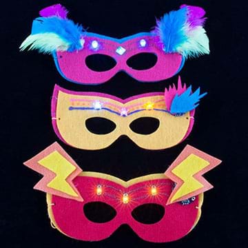 A photograph shows three eye masks made of purple, yellow and pink felt with lighted LEDs above the eye holes, and additional decoration from glued-on feathers and lightning bolt felt cutouts.  