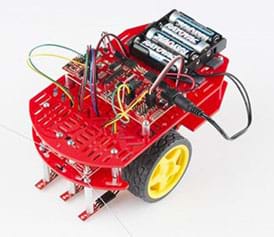 A photograph shows a two-wheeled robot with a two-level red plastic platform covered in oblong holes, on which a circuit board, wires and four batteries are attached to the top level.