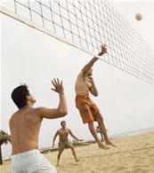A photograph shows three boys in swimming trunks on a beach jumping and using their hands to redirect a volleyball over a net.