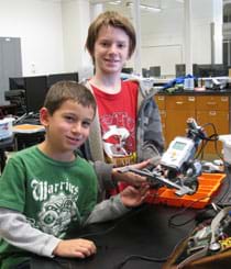 A photograph shows two boys holding the LEGO robot they created.