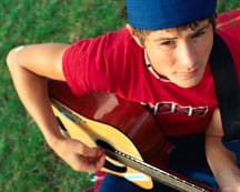 Photo shows a teen playing a guitar.