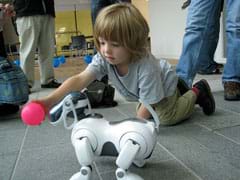 Photo shows child playing with a robot dog (AIBO ERS-7).
