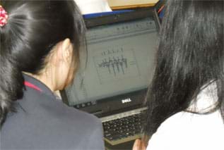 A photograph shows two girls looking at a graph on a laptop screen.