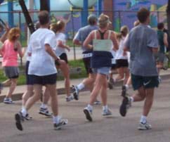 A photograph shows the backs of about 10 people in shorts and T-shirts jogging on a public street in a 5K race.