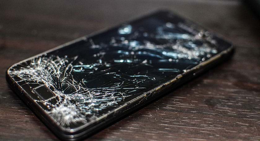 A photograph shows a Samsung Galaxy S2 cellular phone with a heavily cracked black glass display screen, the result of being run over by a Volvo tire.